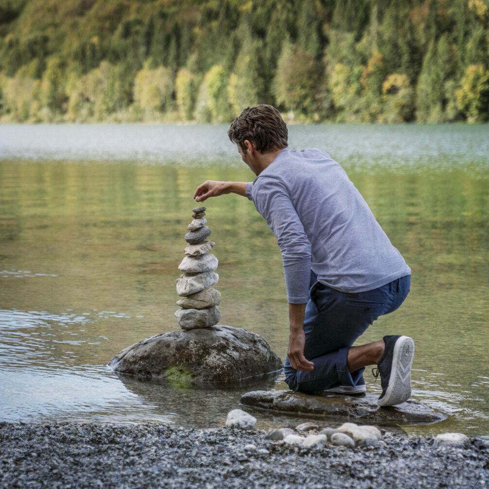Mann baut einen Turm aus Steinen am See